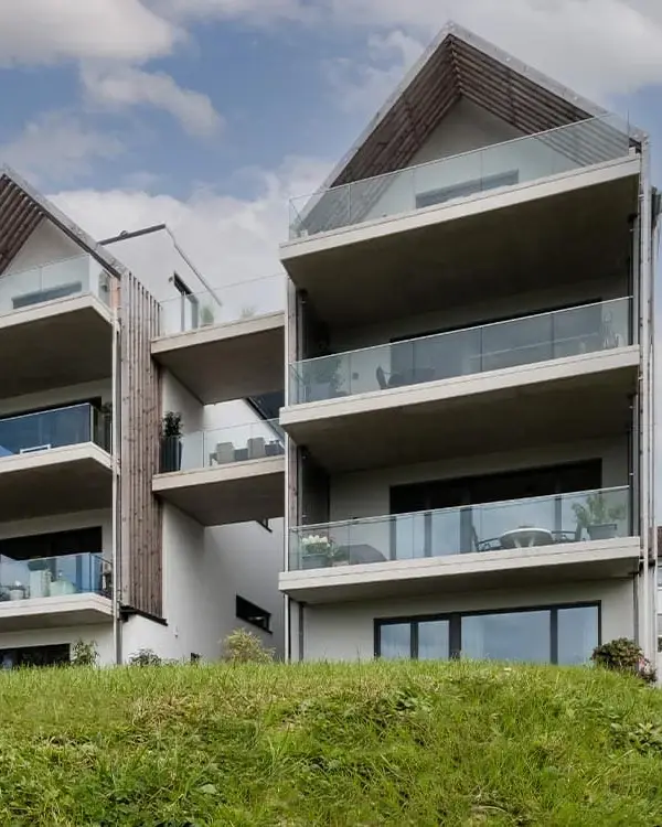 Atriumhaus in Gummersbach-Hülsenbusch: zwei weiße Giebelhäuser mit Glasbrüstungen und seitlichen Holzlamellen, von der Talseite gesehen