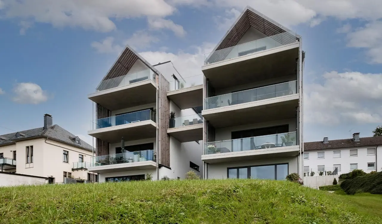 Atriumhaus in Gummersbach-Hülsenbusch: zwei weiße Giebelhäuser mit Glasbrüstungen und seitlichen Holzlamellen, von der Talseite gesehen