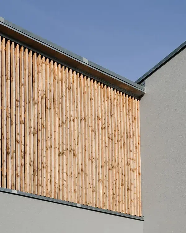 Fassade von Mi49 mit vertikalen Holzlamellen über weißem Putz vor blauem Himmel