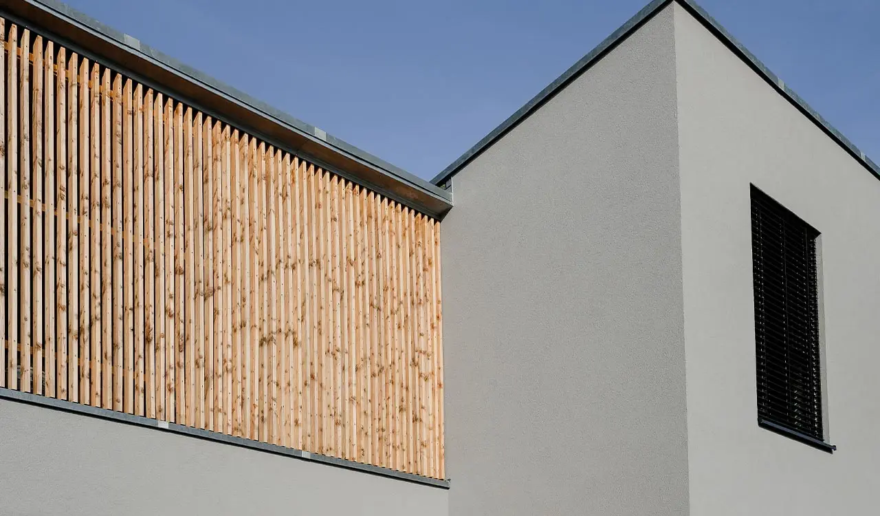 Fassade von Mi49 mit vertikalen Holzlamellen über weißem Putz vor blauem Himmel